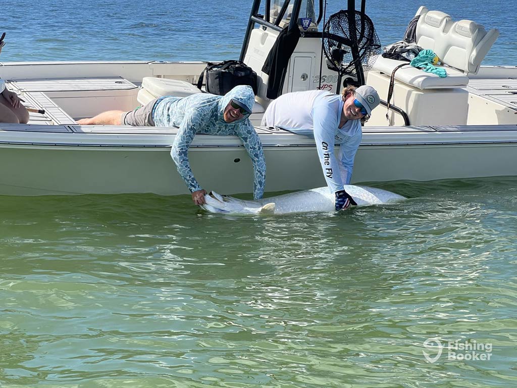 Two anglers leaning over the side of a center console fishing boat in Georgetown, SC, holding a Tarpon partially in the water, while looking towards the camera