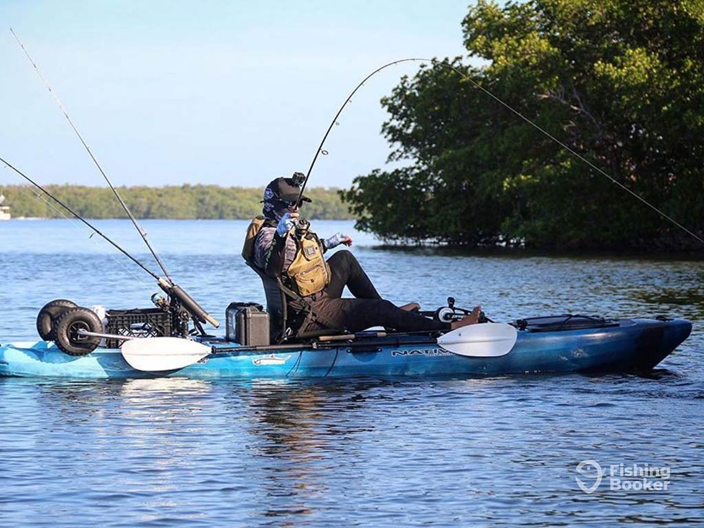 An experienced kayak angler casting into the water, with a couple of rods in the water behind the kayak, trolling, as they pedal the shallow waters of Southwest Florida