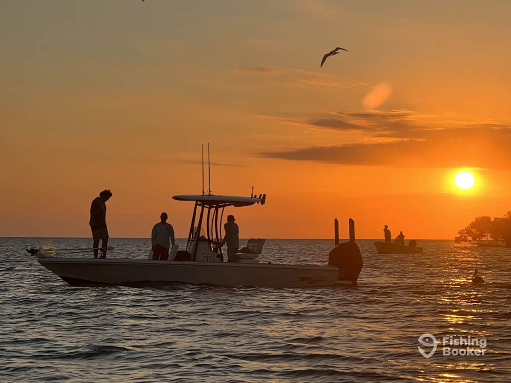 A silhouette of a fishing charter in Georgetown, SC, at sunset, with several people standing around on it on a clear day