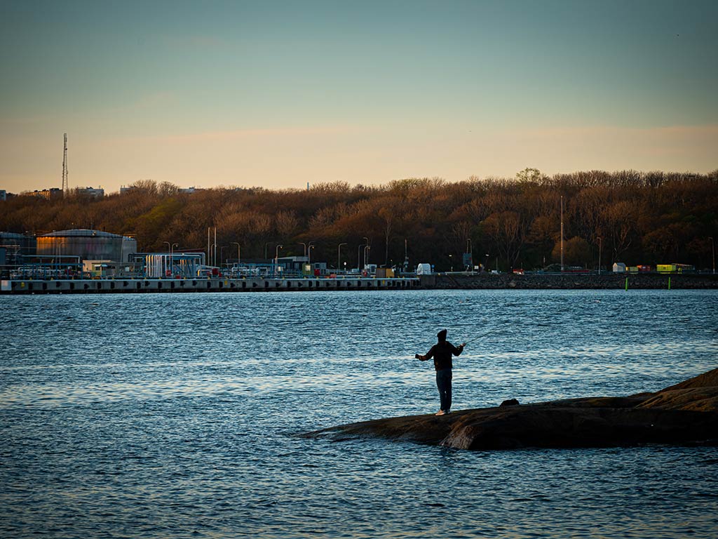 A view from afar of a fly angler casting a line into Cape Cod's inshore waters at sunset