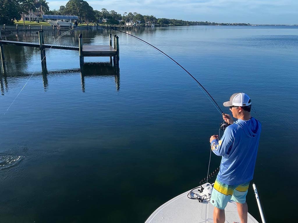 A view from a flybridge of an angler at the front of a boat, casting a fly fishing line into calm waters near Siesta Key on a sunny day