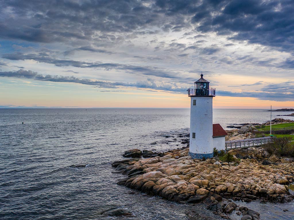 A view from land towards the Atlantic Ocean, with Gloucester lighthouse on the right-hand side of the image near sunset on a cloudy day