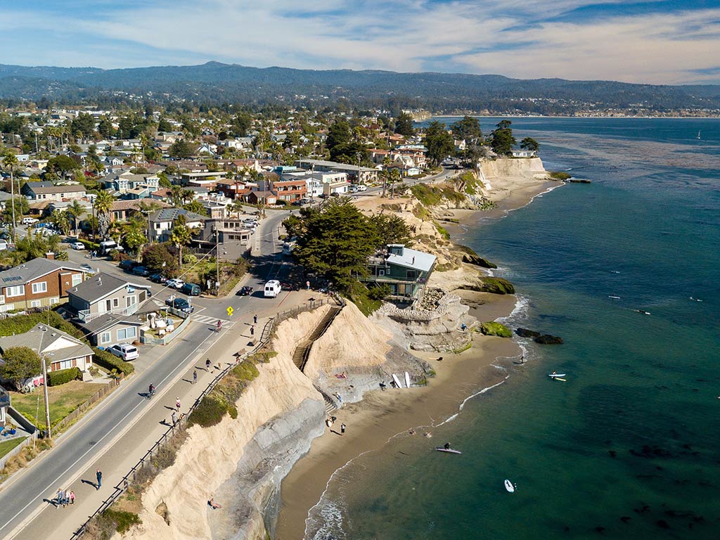 An aerial view of Pleasure Point in Santa Cruz, California, witha beach visible in the foreground and the Pacific Ocean on the right-hand side of the image on a sunny day