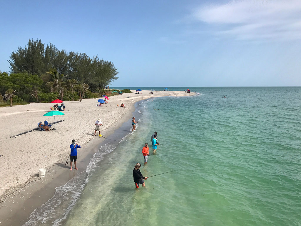 A view along the seafront on Sanibel Island of a group of several anglers casting into the surf, some while wading, on a sunny day