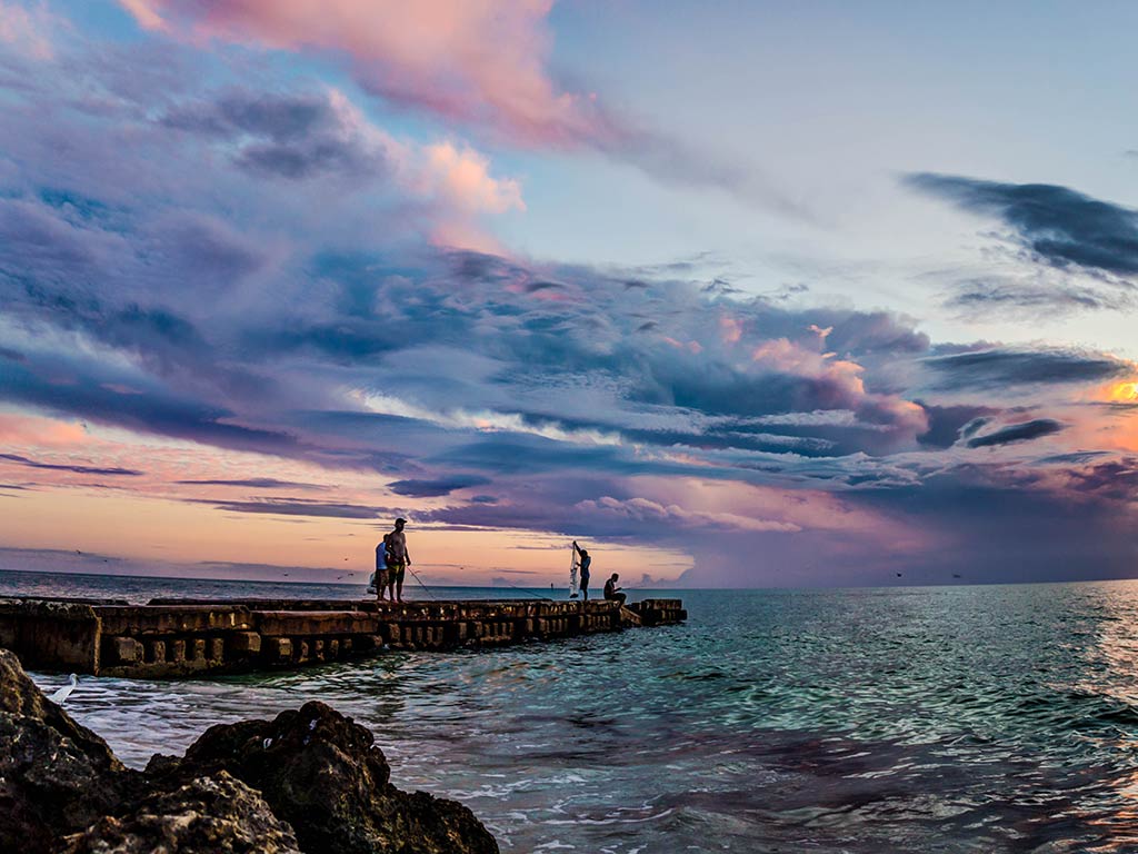 A view from the rocky shoreline towards a jetty where some anglers are packing up their gear at sunset on Florida's Gulf coast