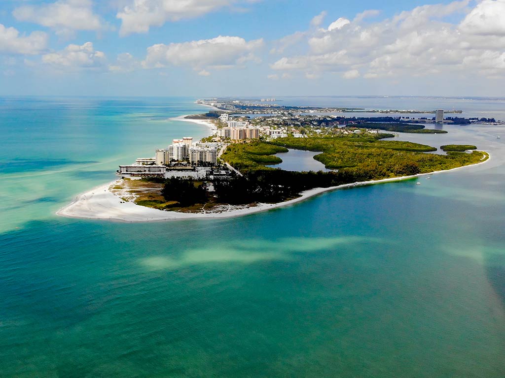 An aerial view of the tip of Siesta Key, with turquoise waters all around and a beach in the middle of the image on a relatively clear day