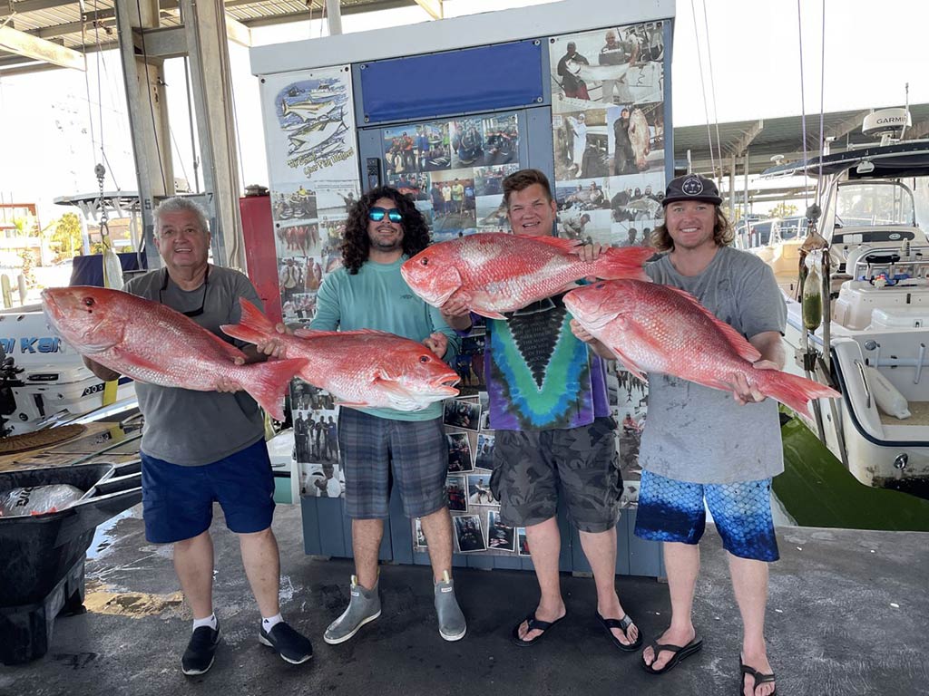 A group of happy anglers back on a covered dock, holding a large Red Snapper each in Texas