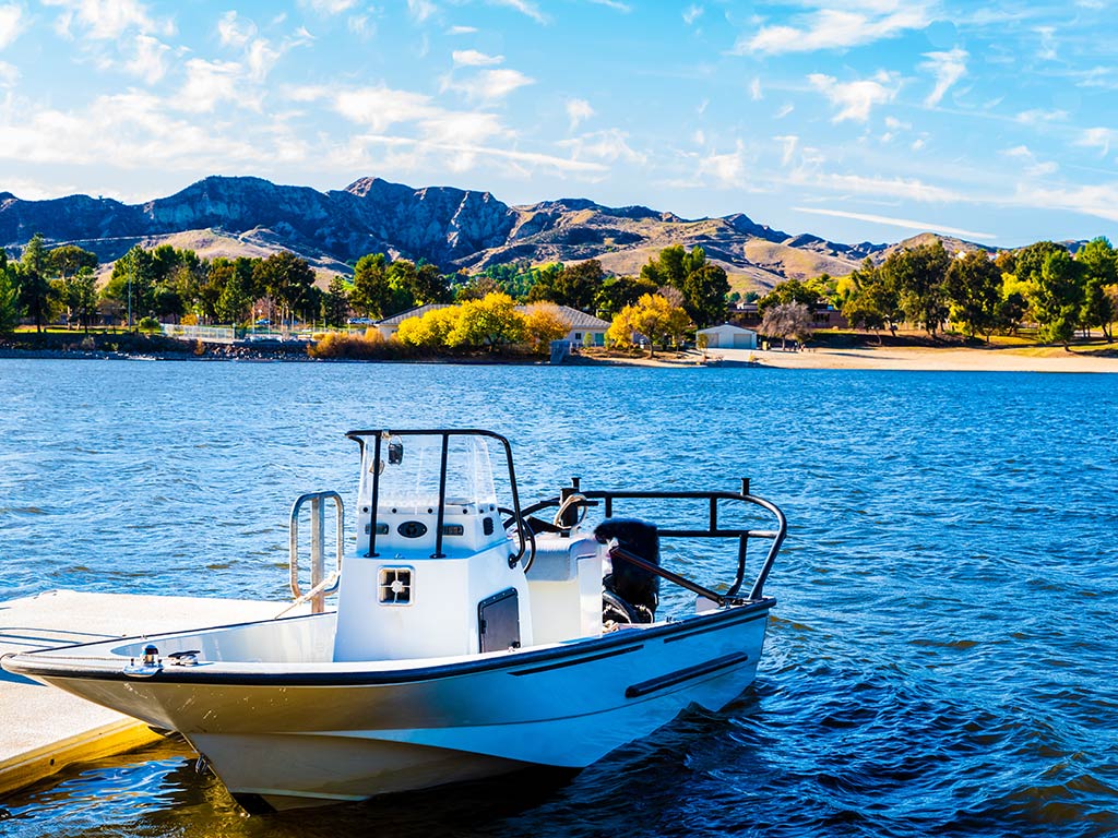 A boat is docked in the foreground on Castaic Lake, with the water, blue skies, and a hill in the distance