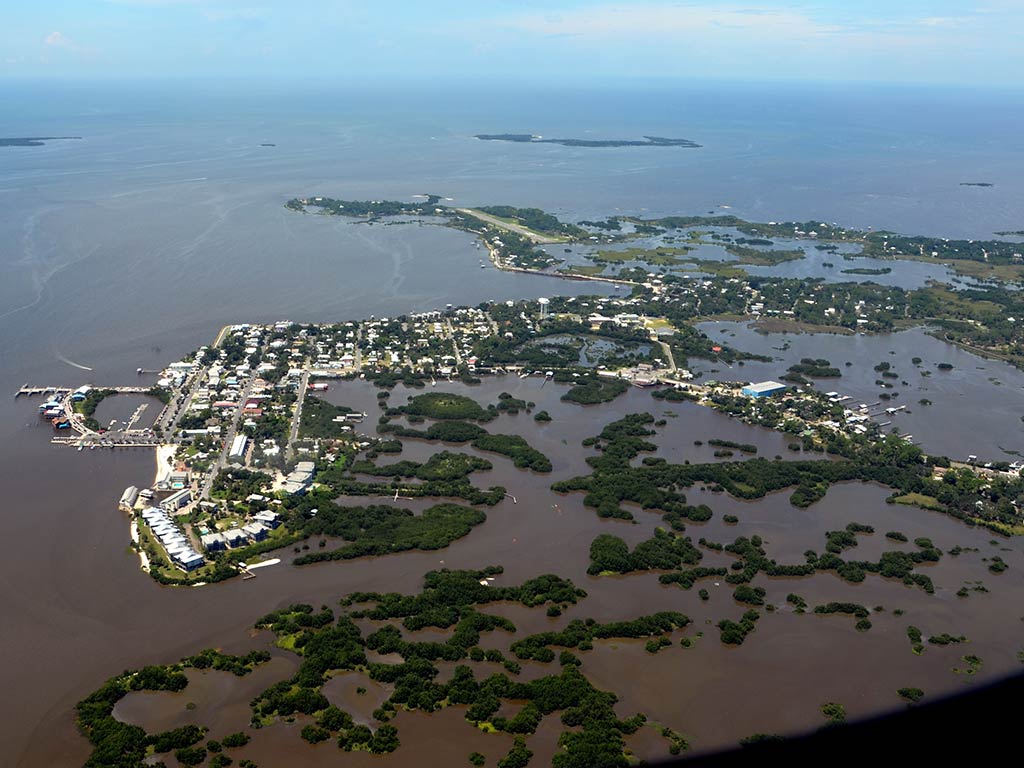 An aerial view of Cedar Key and its surrounding other keys on a murky day, with murky waters and greenery visible, along with some houses