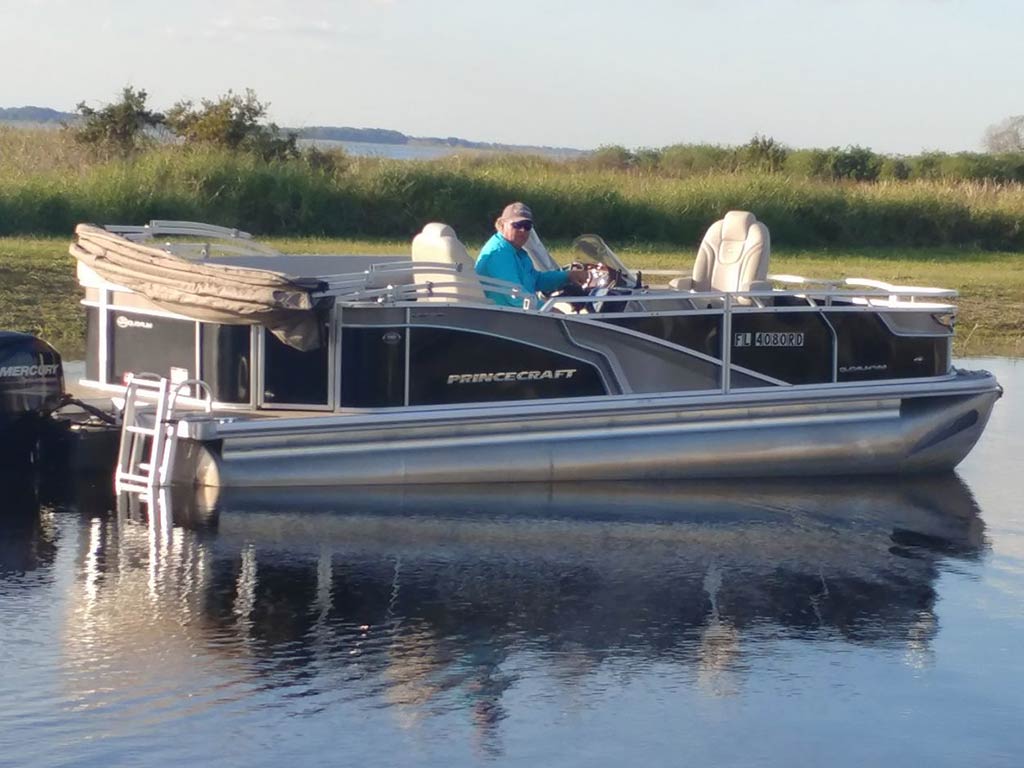 A view across the water of a pontoon fishing charter on Lake Toho, with the captain looking towards the camera and two other people on board on a sunny day