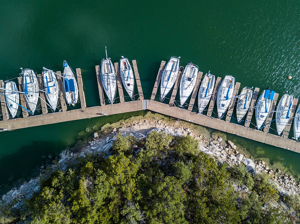 A bird's eye view of several boats docked at a small marina on Lake Travis, Texas