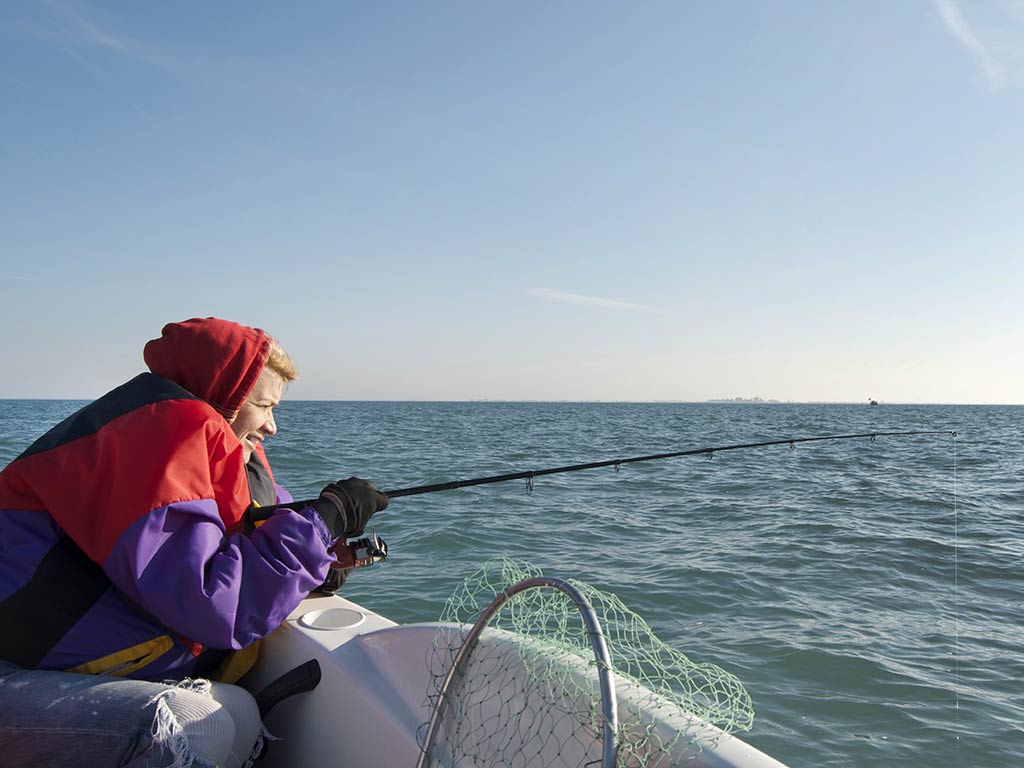 An angler in a winter coat vertically jigging a fishing rod in search of Walleye on a spring fishing charter in the Great Lakes