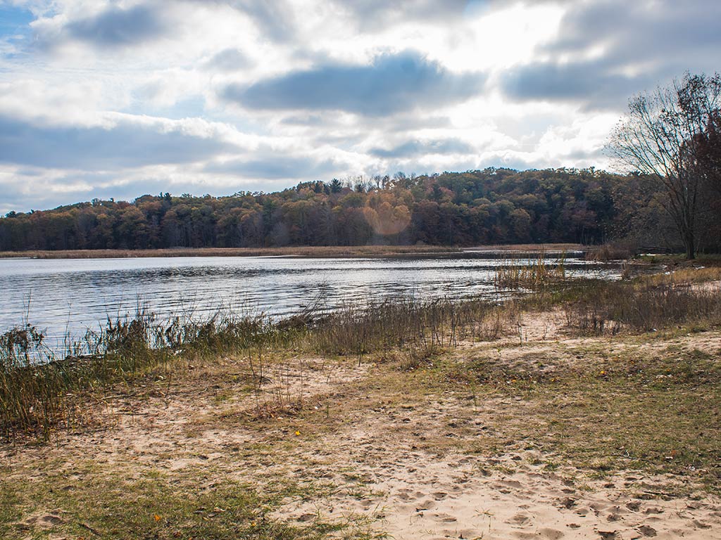 A view from land across a sandy beach on the Muskegon River on a cloudy but dry day, with trees on the shoreline in the distance