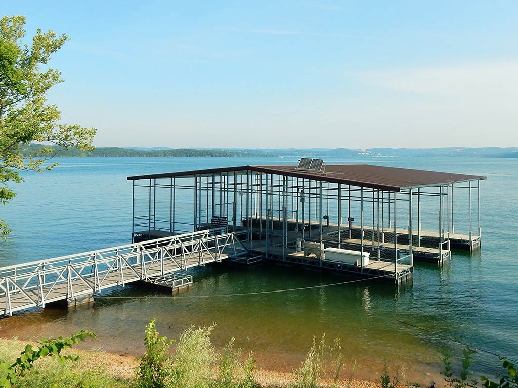 A view of a small, covered fishing pier on Table Rock Lake on a clear day, with a tree visible to the left of the image and the water visible all the way to the horizon in the distance on a clear day