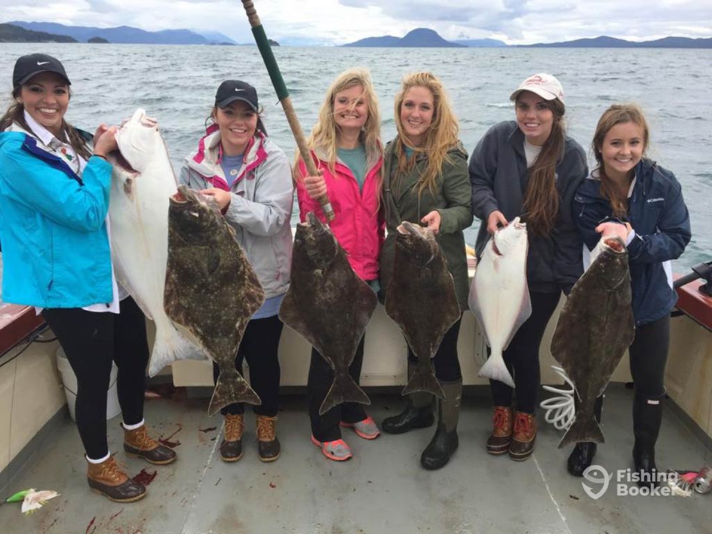 A group of female anglers aboard a sportfishing boat in Juneau, AK, each holding up a Halibut with the waters behind them on a cold day