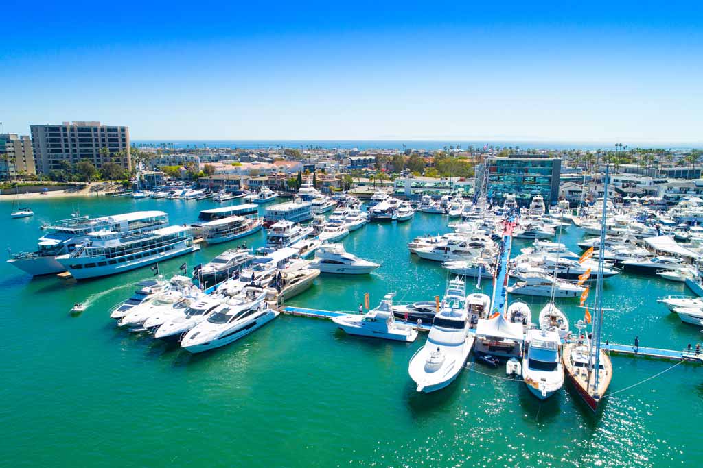 A view of one of the marinas in Newport Beach, California, with rows of boats docked on turquoise waters, with blue skies in the background