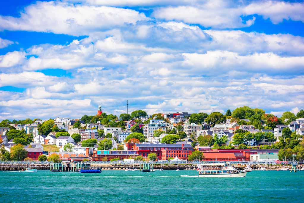 A view of the colorful houses and buildings of Portland, Maine from the turquoise waters of the Atlantic with a blue sky and white clouds in the background