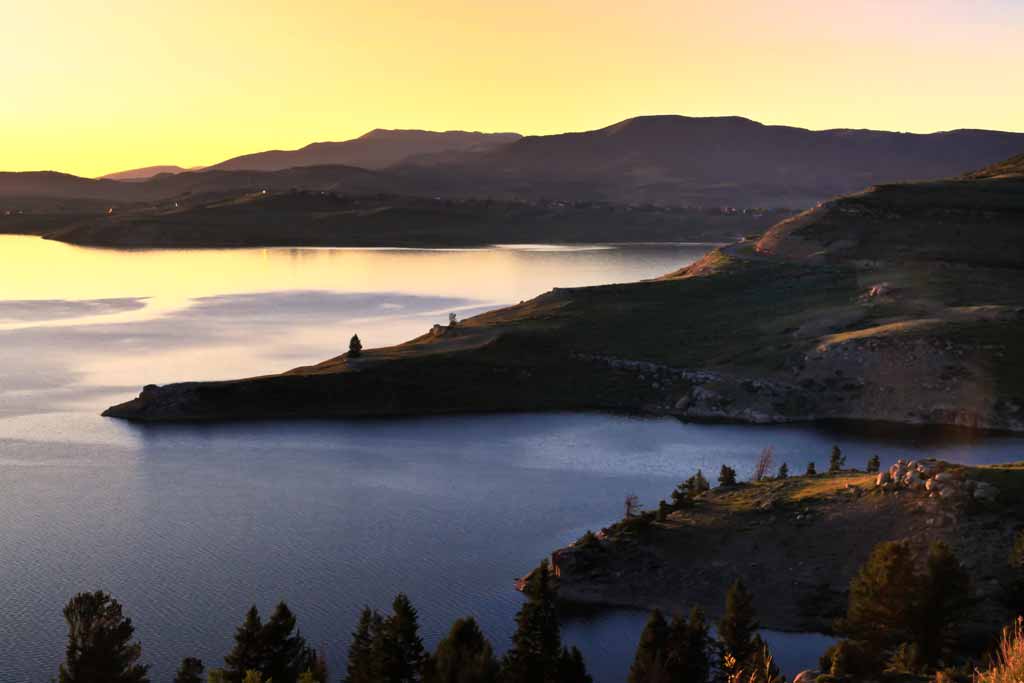 An aerial view of Strawberry Reservoir in Utah at sunset, with most of the land covered in shadow and the water reflecting sunlight