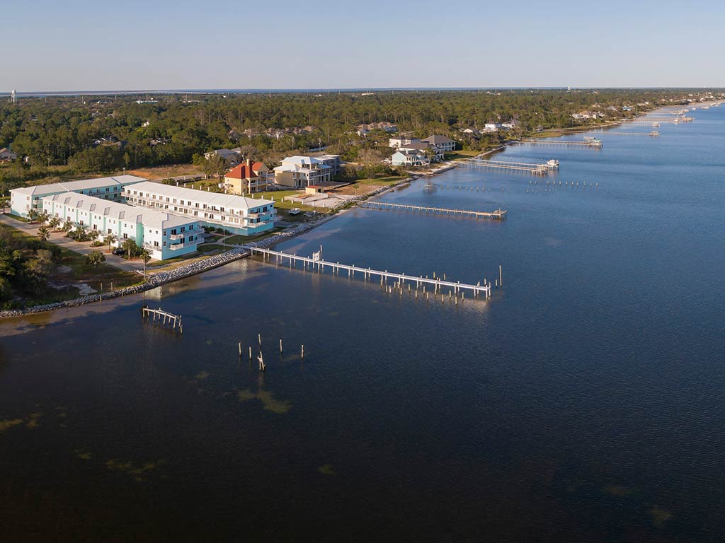 An aerial view of the waterfront on the bay or sound in Navarre, with a few docks and piers extending out into the water on a sunny day