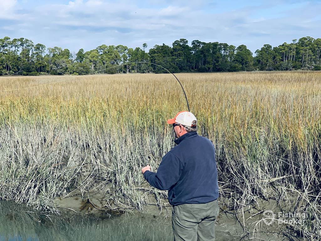 A view from behind of an angler casting a fly fishing line in the flats of South Carolina on a cloudy day