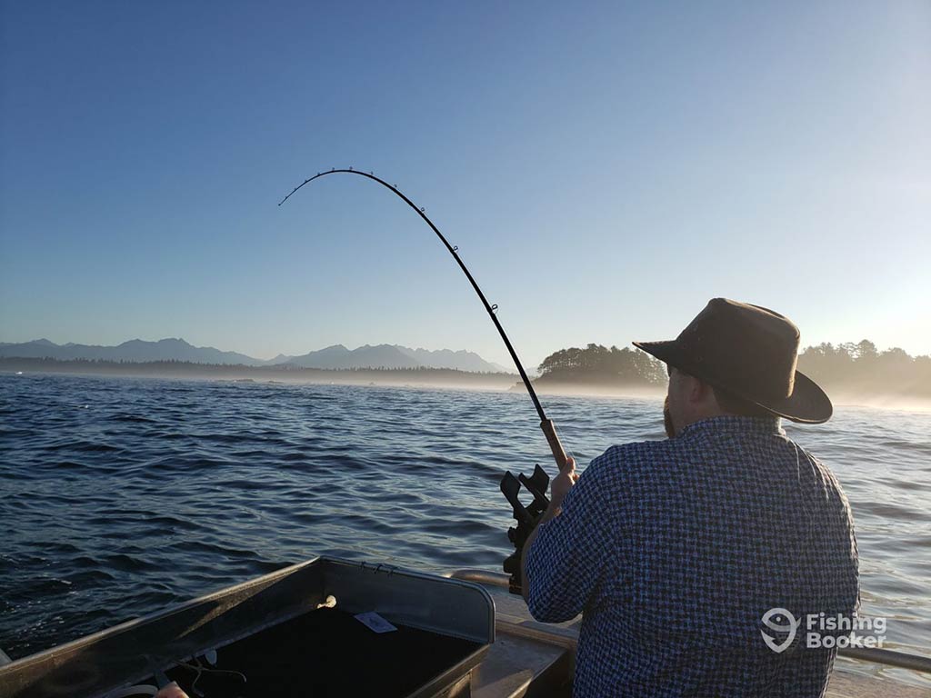 A rearview image of an angler in a hat bottom fishing aboard a fishing charter in Ucluelet at dusk on a sunny day