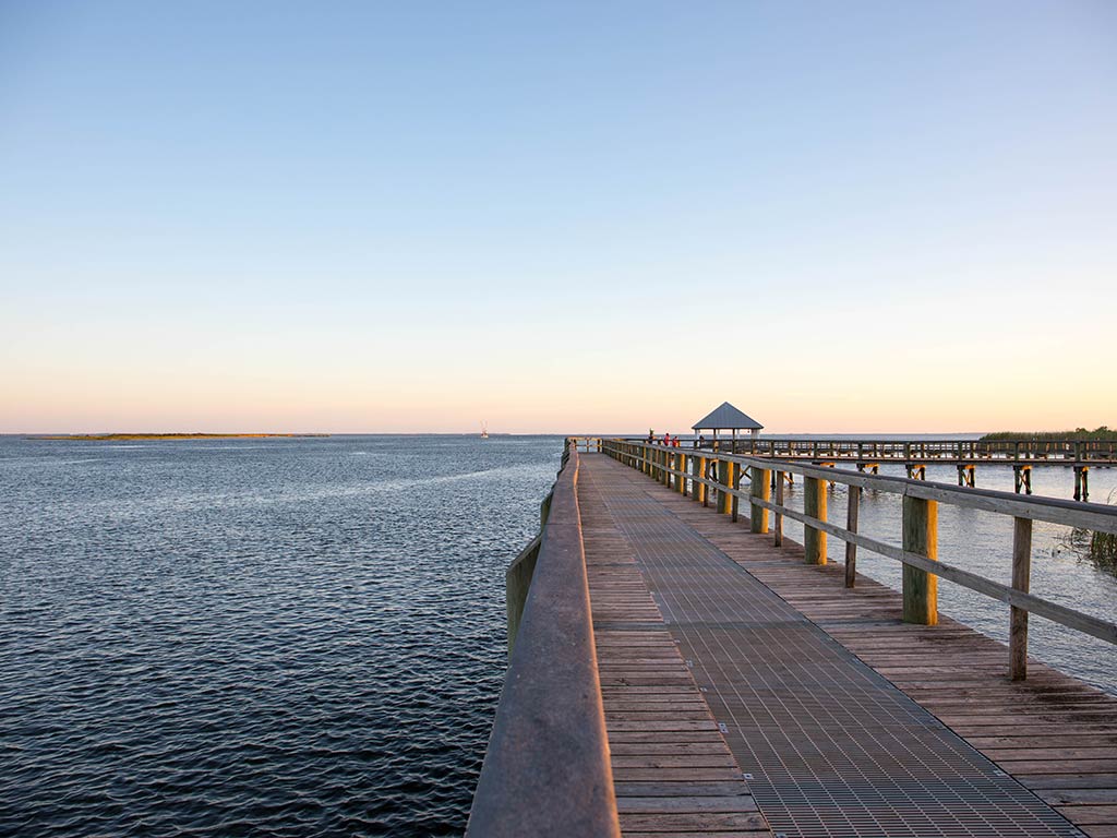 A view along a fishing jetty in Apalachicola near sunset, with the hetty on the right of the image and the sea on the left