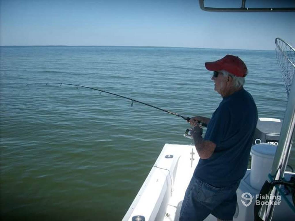 An angler in a baseball cap and sunglasses casts their line off the side of a boat near Apalachicola on a sunny day