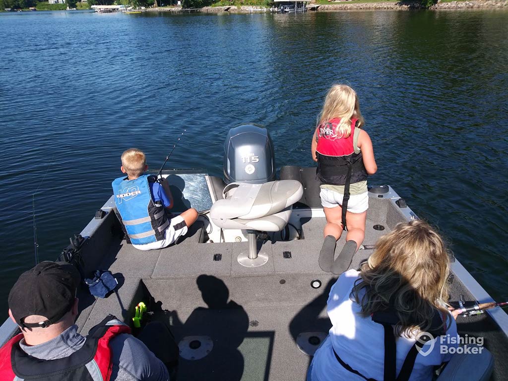 A view from behind of a family fishing on the deck of a boat in the Mississippi River on a sunny day, with calm waters all around them