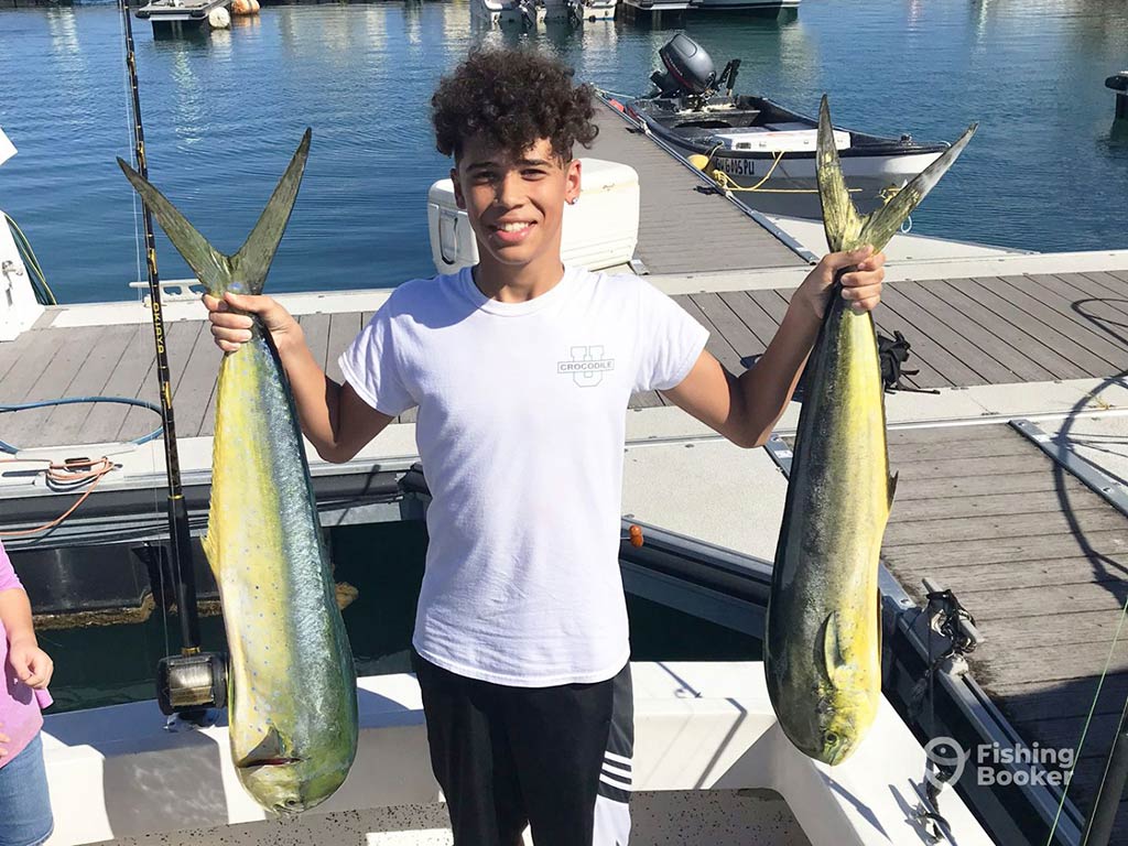 A youthful angler holds two Mahi Mahis aboard a boat back at the dock in Apalachicola after a successful fishing trip on a sunny day