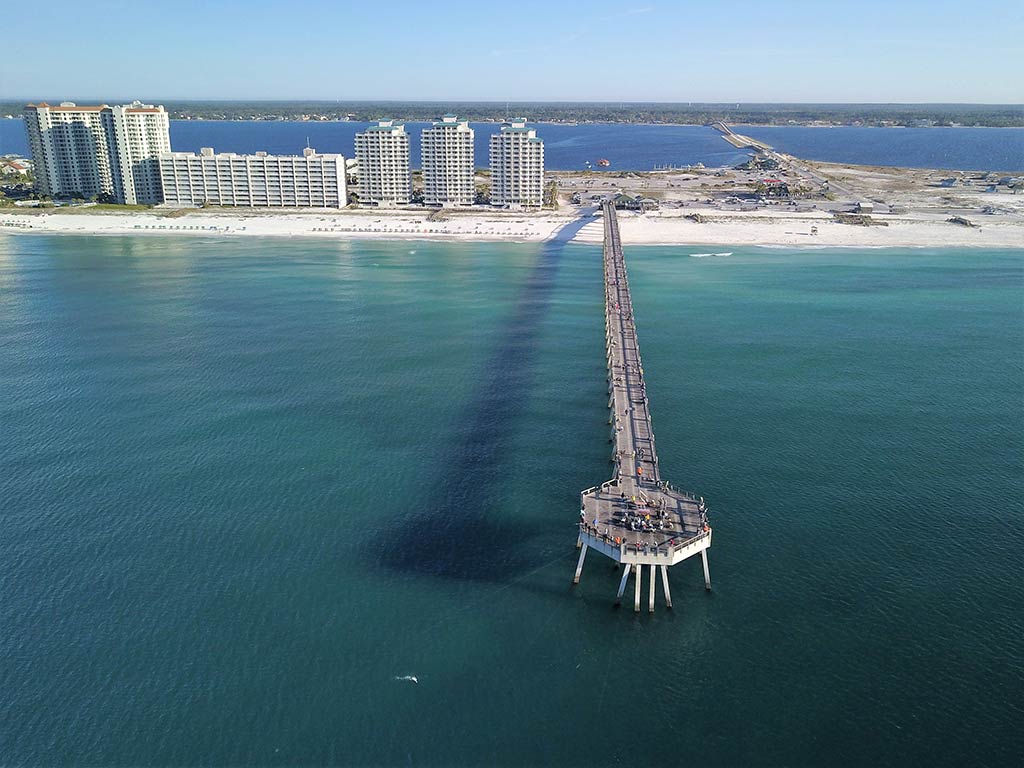 An aerial view looking towards the beach and town of Navarre, with the legendary fishing pier in the foreground sticking out into turquoise waters on a sunny day