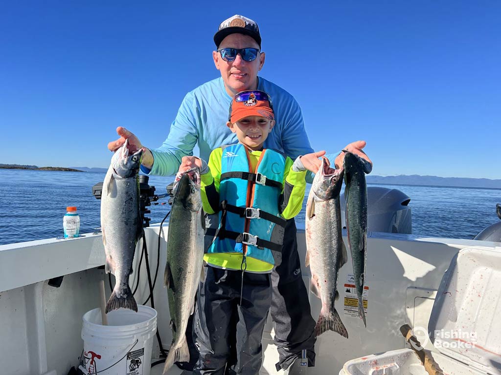 A father and son on a fishing charter, holding four Salmons caught fishing near Juneau, AK, on a sunny day