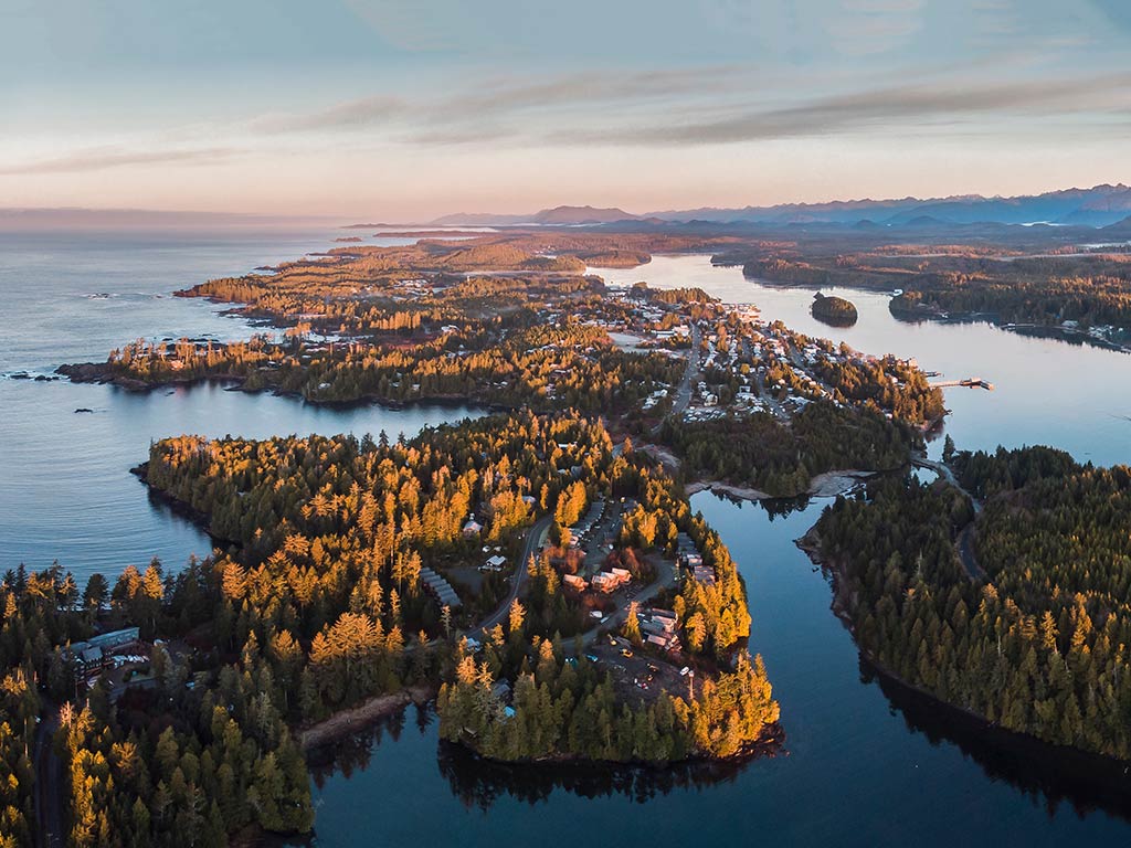 An aerial view of Ucluelet at sunset, with green trees visible on land and the waters of the Pacific working their way around it