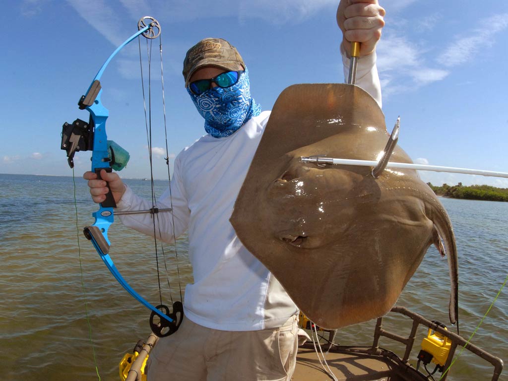 A photo of an angler holding bow in one hand and a Ray in other that was caught while bowfishing