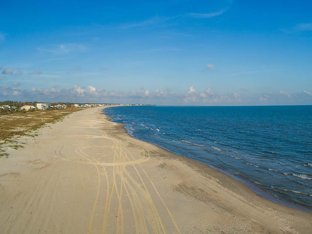 A view along a beach in Cape San Blas, with the waters of the Gulf of Mexico on the right of the image and clear, yellow sands dominating the image on a clear day