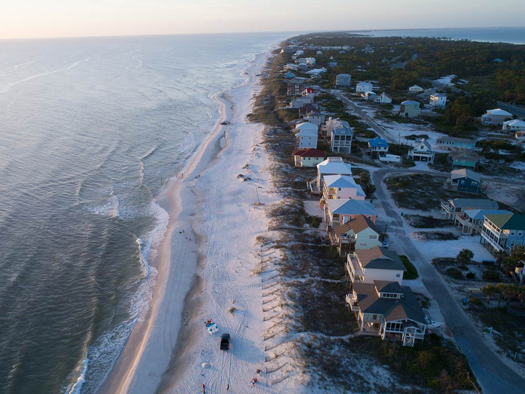 An aerial view of a beach leading towards the tip of Cape San Blas at sunset, with the waters of the Gulf of Mexico on the left of the image, the beach in the middle, and residential buildings on the right