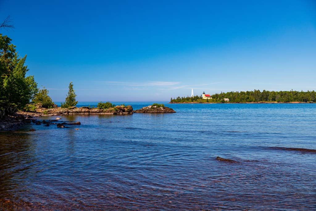 A view of clear skies and the calm waters of Lake Superior from the Keweenaw Peninsula, which is one of the best Fourth of July fishing destinations, with the Copper Harbor lighthouse visible in the distant background.