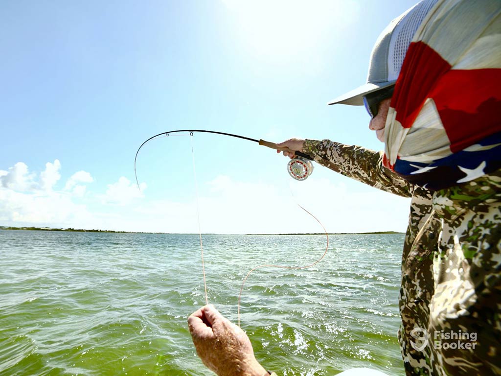 A closeup of an angler casting a fly fishing rod with one hand and holding his line in the other hand on a clear day in the clear flats of San Pedro, Belize