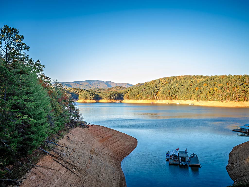 A view from the shores of Fontana Lake, NC, one of the best Bass fishing spots in the state, on a clear day, with tree-lined shores visible all around the still water