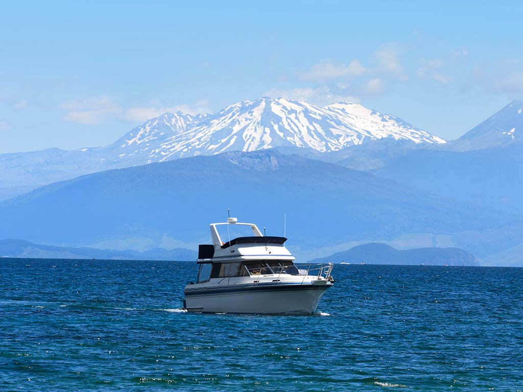 A view across Lake Taupō towards a large, offshore sportfishing vessel with a volcanic mountain covered in snow in the distance on a clear day