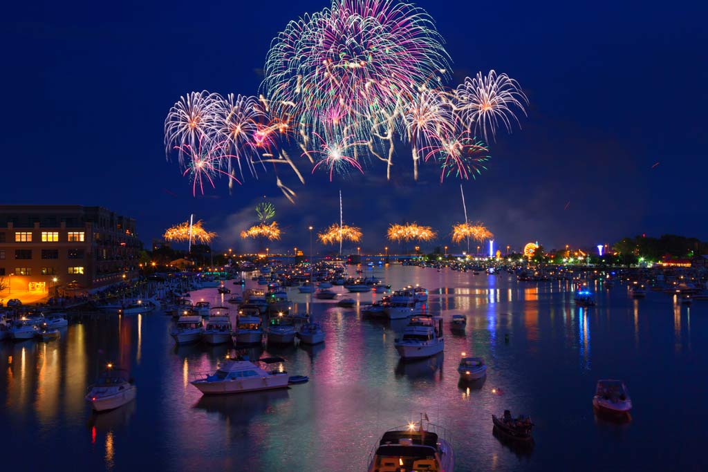 A Fourth of July fireworks parade in Saginaw Bay, Michigan, with numerous boats in the water made visible by the fireworks light.