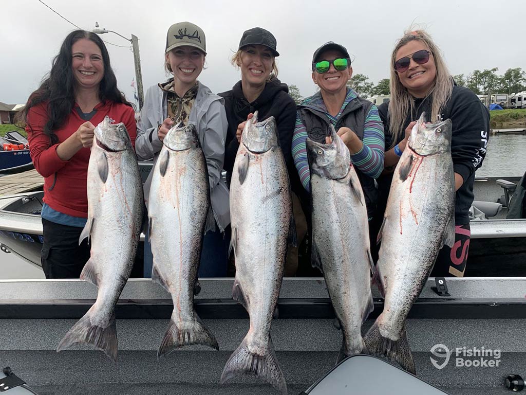 A group of female anglers posing at the side of a fishing boat with a Salmon each after casting a line in Washington on a grey day