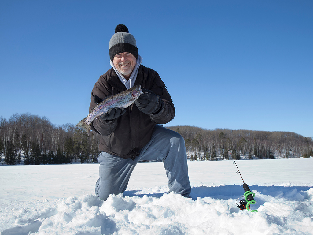 Happy middle aged ice fisherman holds up freshly caught Rainbow Trout on a Minnesota lake north of Grand Rapids