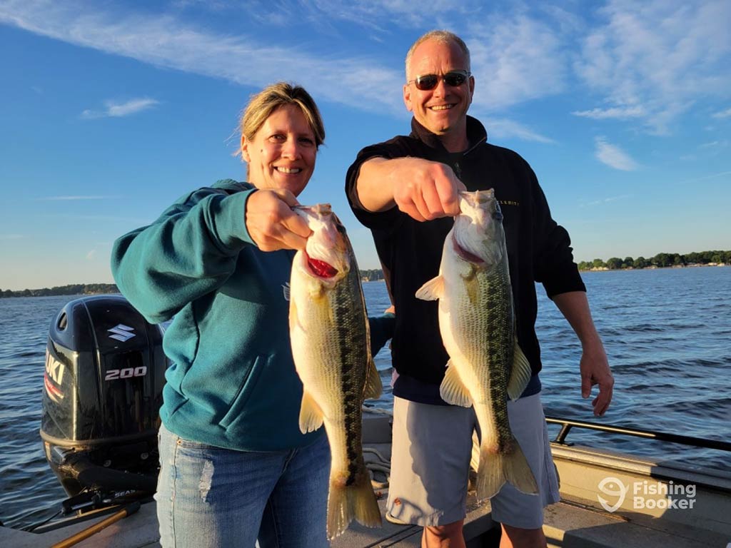 Two middle-aged anglers – one male, one female – holding up a Largemouth Bass each, caught while fishing in North Carolina on a sunny day