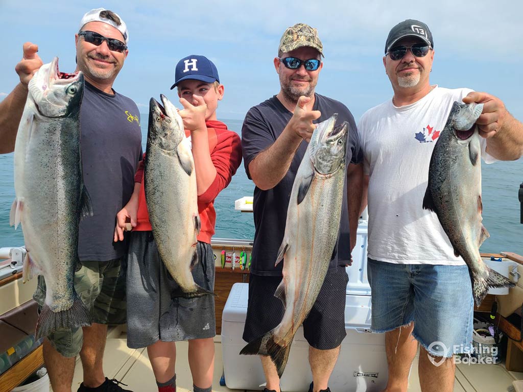 A group of four male anglers of different ages hold up a Salmon each, caught while fishing in St.Catherines, Ontario during summer