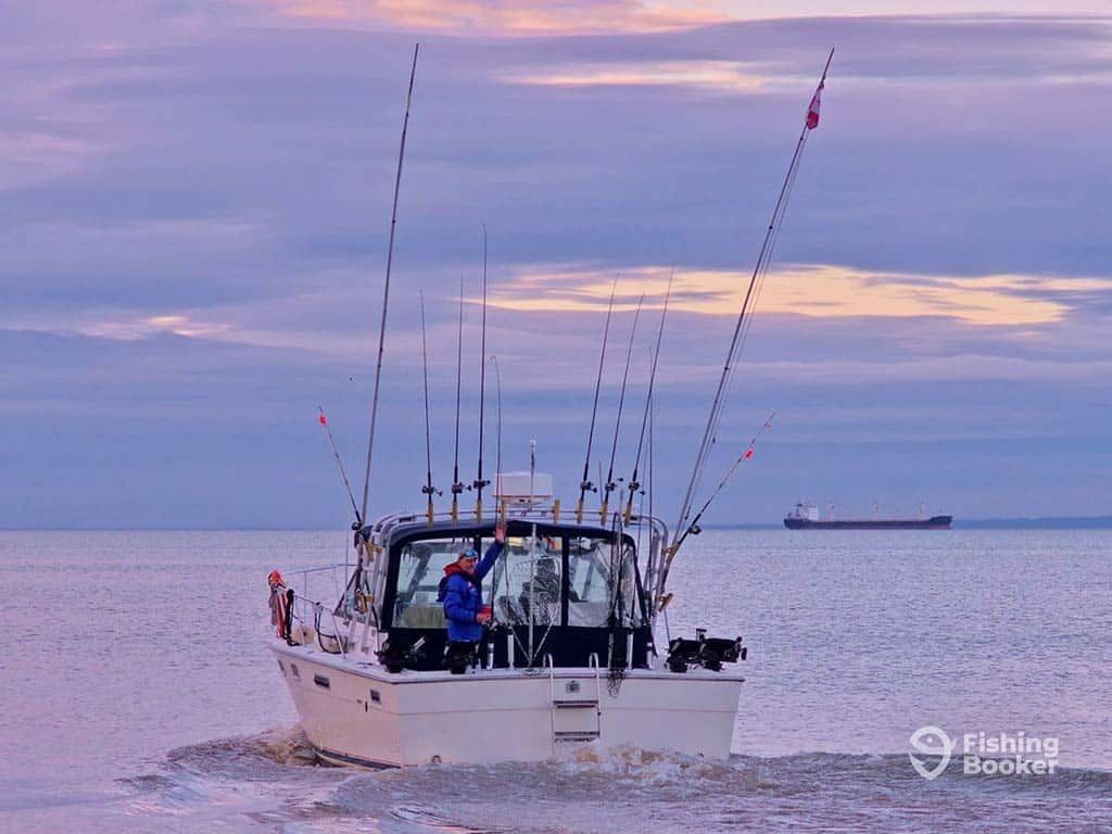 A view across the water towards a fishing charter, fully set up with a number of downriggers for trolling the waters of Lake Ontario near St. Catherines, at sunset on a cloudy day