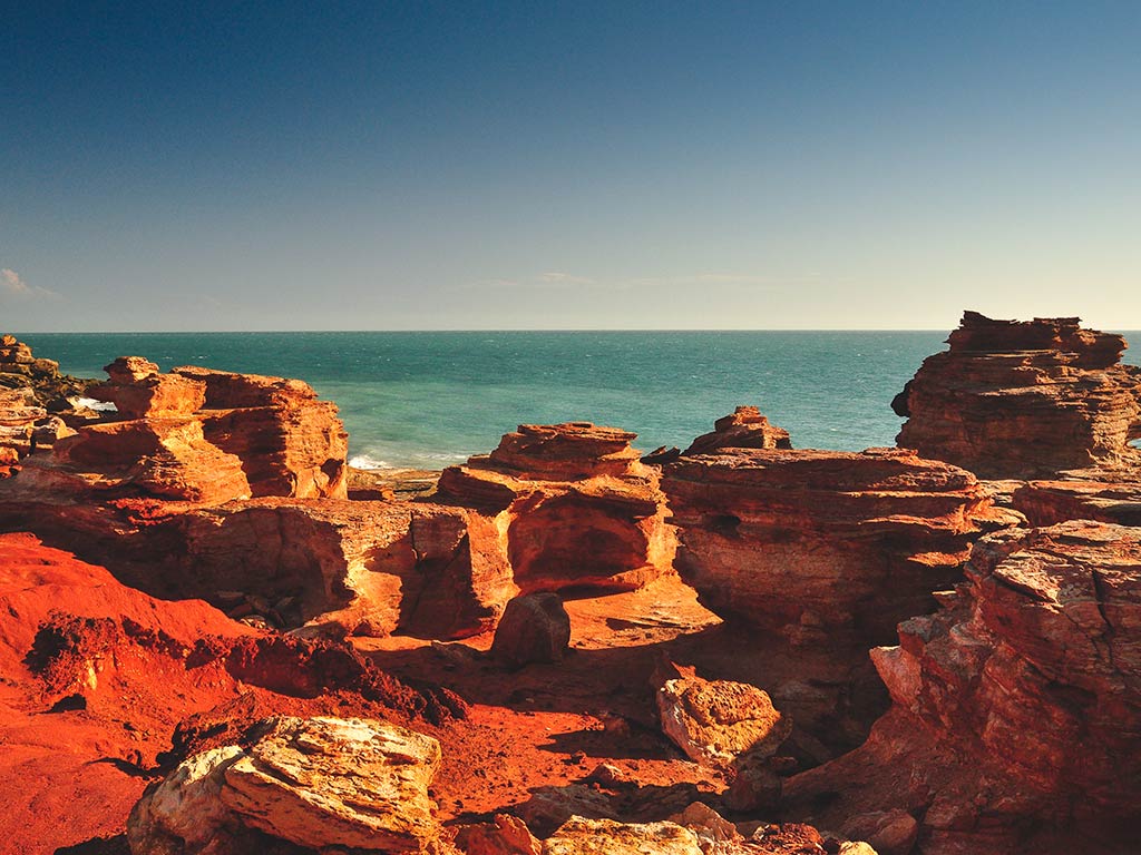 A view across a red rocky shoreline towards the Pacific Ocean in Broome, Western Australia on a sunny day