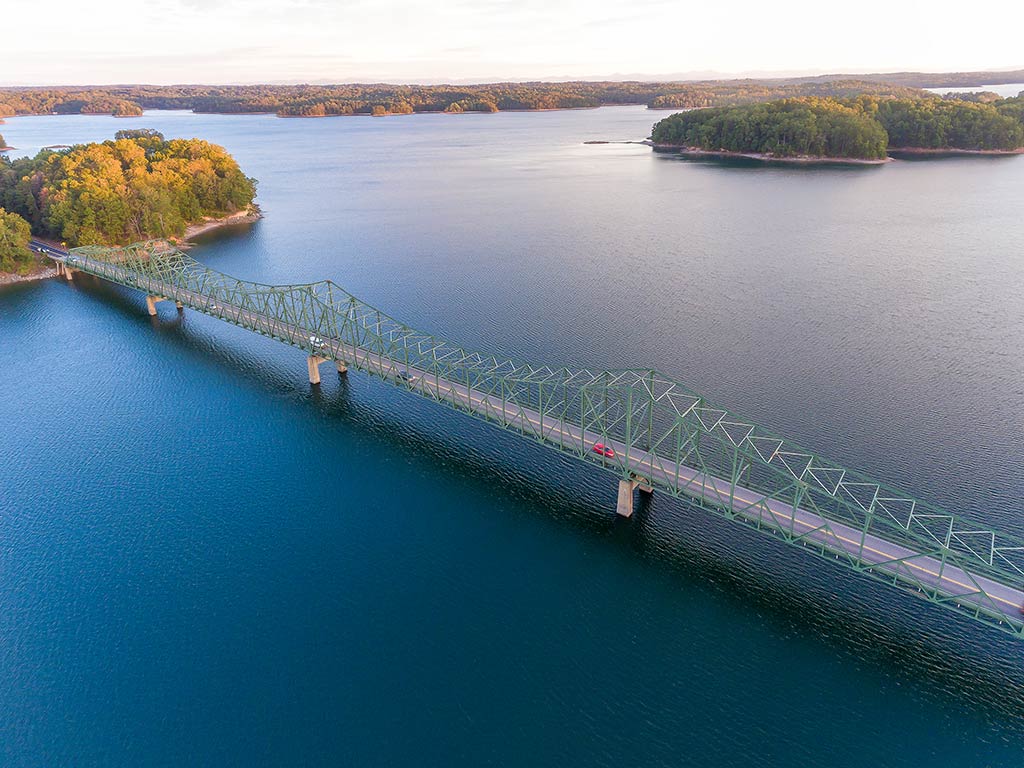 An aerial view of Browns Bridge, crossing Lake Lanier on a clear day, with an island and tree-lined shores visible in the distance