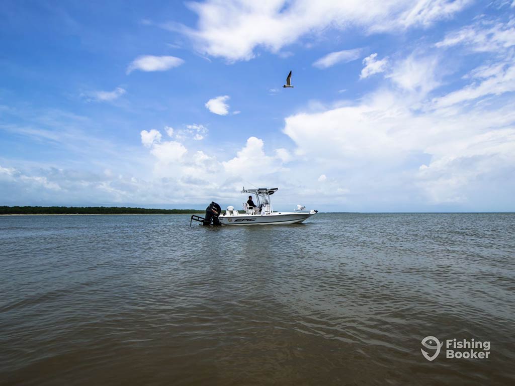 A lone, center console fishing charter peruses the inshore fishing grounds of Cape San Blas, dominating the center of the image, with blue skies, pierced by a few clouds above