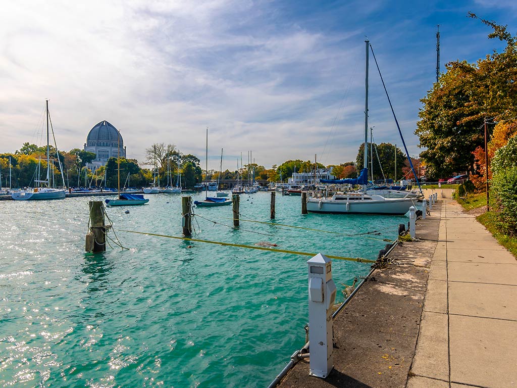 A view from a harbor in Chicago across crystal clear blue water towards a domed building in the distance on a clear day, with some boats visible on the right of the image