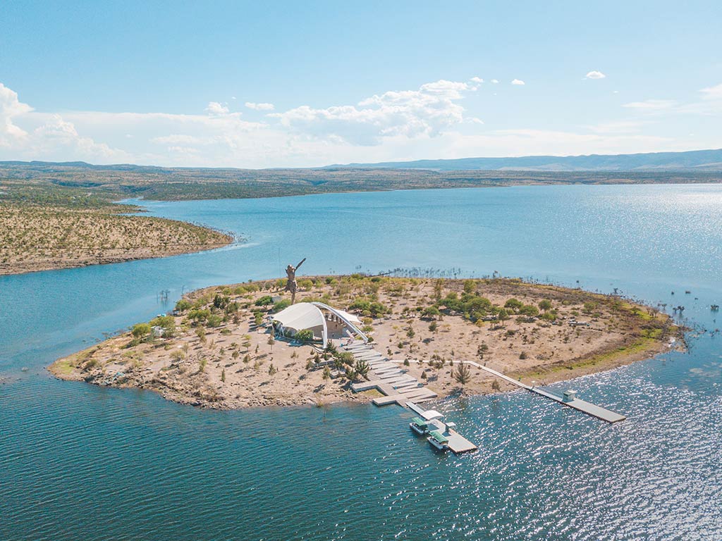 An aerial view of an island in El Cristo Roto Lake in Mexico with a statue visible on the island on a clear day